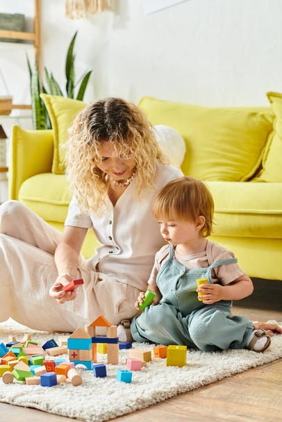 Kędzierzawa matka bawi się radośnie ze swoją córeczką na podłodze w domu, używając metody Montessori.. - Zdjęcie, obraz