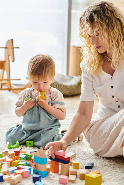 Egy göndör anya és kislánya játékosan kommunikálnak a padlón a Montessori oktatási módszerrel.. - Fotó, kép