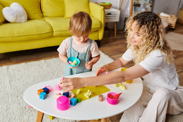 A loving mother plays with her curly toddler daughter in a warm living room, engaging in Montessori educational activities. - Photo, Image