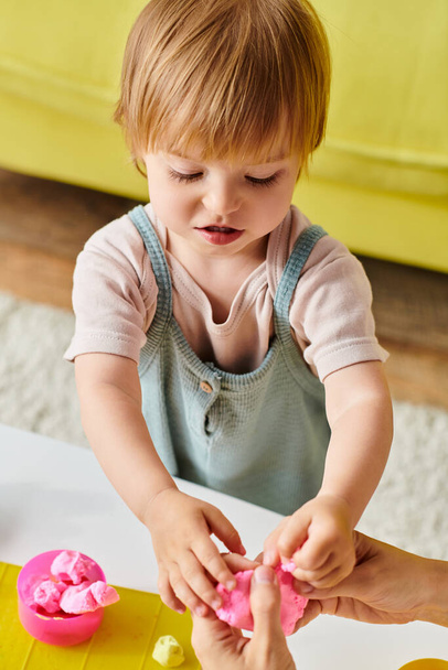 Ένα μικρό παιδί παίζει ευτυχισμένα με μια ζύμη, εξερευνώντας τη μέθοδο εκπαίδευσης Montessori στο σπίτι. - Φωτογραφία, εικόνα