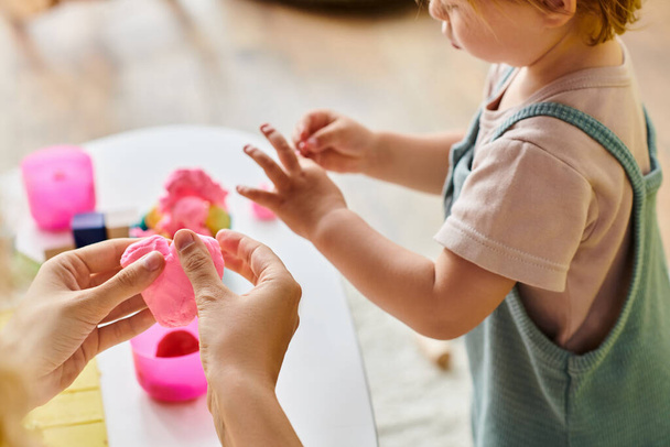 mother guides her toddler daughters hand over a table, engaging in a Montessori education activity at home. - Photo, Image