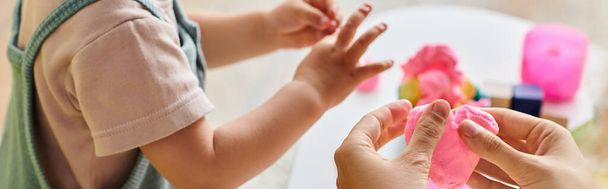 Curly-haired mother guides toddler daughters hand holding pink object, embracing Montessori education at home. - Photo, Image