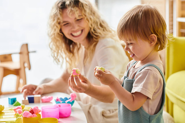 Μια σγουρή μητέρα και η κόρη της ασχολούνται με τη μέθοδο εκπαίδευσης Montessori στο σπίτι, εξερευνώντας και παίζοντας σε ένα τραπέζι. - Φωτογραφία, εικόνα