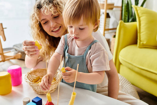 Μια σγουρομάλλα μητέρα και η μικρή της κόρη μαθαίνουν δημιουργικά με ξηρά ζυμαρικά χρησιμοποιώντας τη μέθοδο Montessori στο σπίτι. - Φωτογραφία, εικόνα