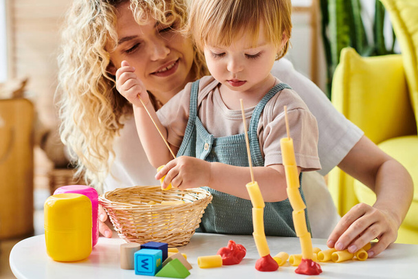 Kiharatukkainen äiti ja hänen taaperonsa tytär ovat leikkisästi vuorovaikutuksessa kotona olevien opettavaisten Montessorin lelujen kanssa.. - Valokuva, kuva