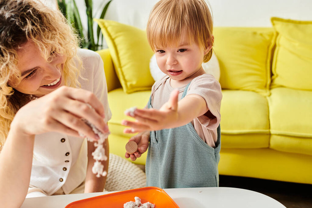 Kręcone matka i jej córka maluch żartobliwie badać i eksperymentować z różnych przedmiotów spożywczych przy użyciu metody edukacji Montessori w domu. - Zdjęcie, obraz