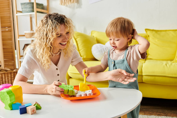 Une mère aux cheveux bouclés s'engage activement avec sa fille en bas âge en utilisant la méthode Montessori à une table. - Photo, image
