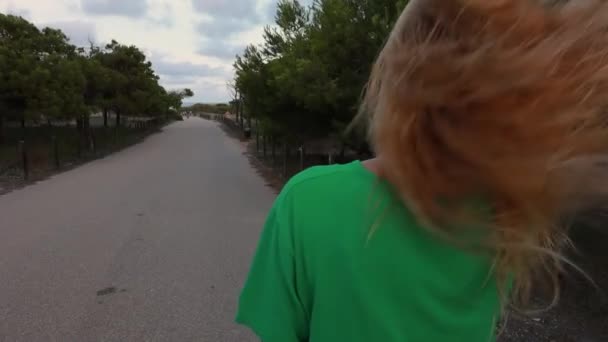 νεαρή γυναίκα με μακριά μαλλιά τρέχει σε ένα πράσινο πάρκο - Πλάνα, βίντεο