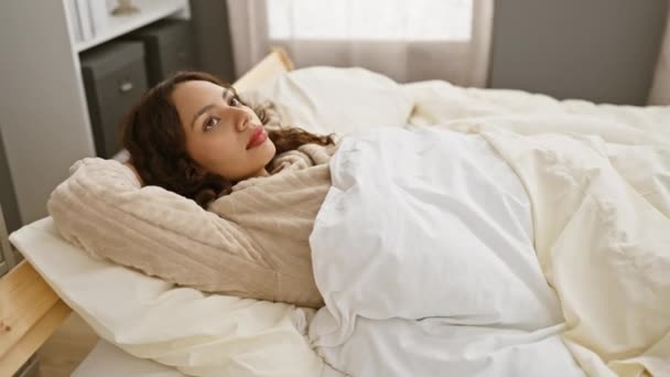 Mladá žena odpočívá ve své útulné ložnici, uhnízděná v posteli s bílým povlečením a měkkými polštáři. - Záběry, video
