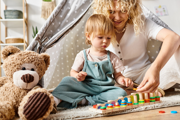 Egy göndör hajú anya aktívan játszik és tanul a kislányával otthon a padlón, a Montessori módszerrel.. - Fotó, kép