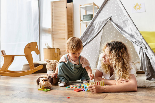 Kıvırcık saçlı bir anne ve küçük kızı, Montessori metodunu takip ederek, eğitici oyuncaklarla yaratıcı bir oyun oynuyorlar.. - Fotoğraf, Görsel
