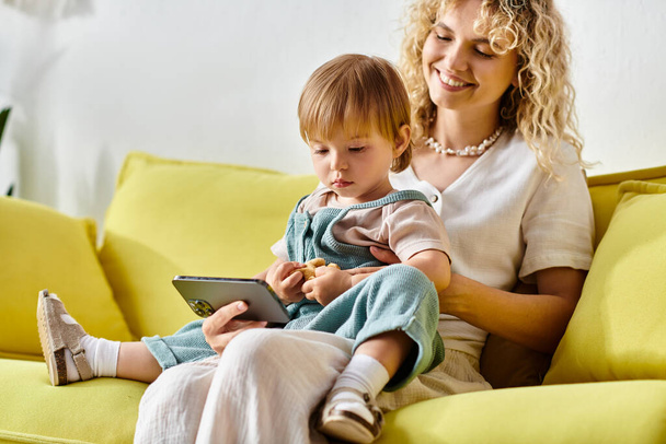 Una madre riccia seduta su un divano con sua figlia in grembo, godendo di un momento accogliente a casa. - Foto, immagini