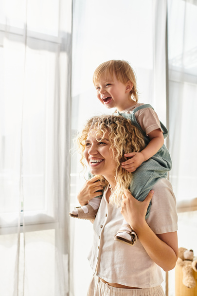 Uma mãe de cabelos encaracolados embala sua filha criança amorosamente em seus braços em casa. - Foto, Imagem