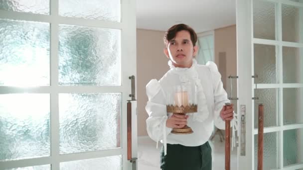Homem de camisola branca segurando uma lanterna de vela, entrando em uma sala através de portas de vidro fosco durante o dia - Filmagem, Vídeo