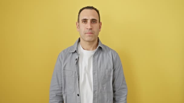 Jonge Latijns-Amerikaanse man met een shirt aan, kijkend in shock, gezicht en ogen bedekkend met de hand, kijkend door vingers met beschaamde uitdrukking. over geïsoleerde gele achtergrond - Video