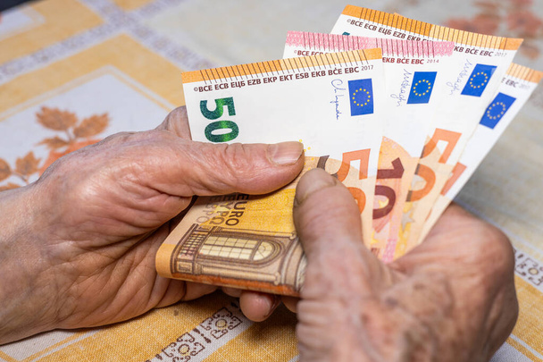 Ikääntyneiden kotitalouksien budjetti euroalueen maissa. Taloudellinen käsite, Eläkeläisnainen pitää useita 50 ja 10 euroseteleitä käsissään, Taloudellinen tilanne vanhusten - Valokuva, kuva
