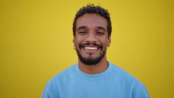 Ritratto di un giovane uomo latino allegro con un sorriso radioso che guarda la macchina fotografica con un'espressione felice, sullo sfondo di una parete gialla. Persone con espressione positiva - Filmati, video