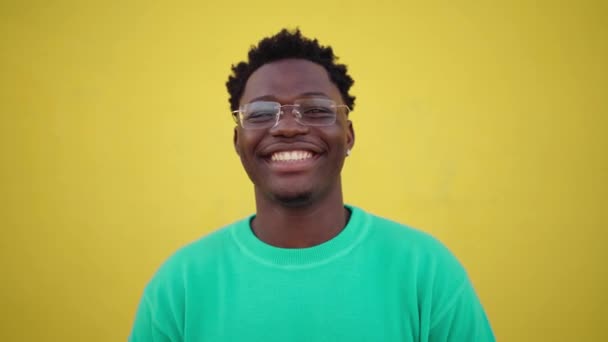 Portret van een jonge vrolijke Afrikaan met een stralende glimlach naar de camera kijkend met een vrolijke uitdrukking, tegen een gele muurachtergrond. Mensen met positieve expressie - Video