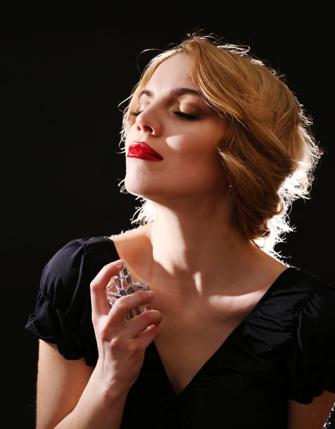 Красива молода жінка з пляшкою парфумів на чорному тлі
 - Фото, зображення