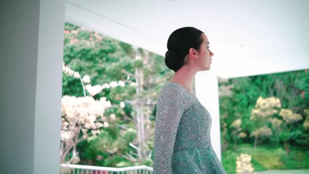 Serene woman standing on a balcony with a lush green backdrop, contemplating nature during the morning - Footage, Video