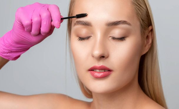 Make-up kunstenaar kamt en plukt wenkbrauwen na het verven in een schoonheidssalon.. - Foto, afbeelding
