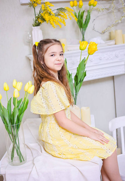 Una bella ragazza in un abito giallo sullo sfondo di mazzi di tulipani gialli. Congratulazioni per la festa della mamma, Festa della donna, 8 marzo. - Foto, immagini