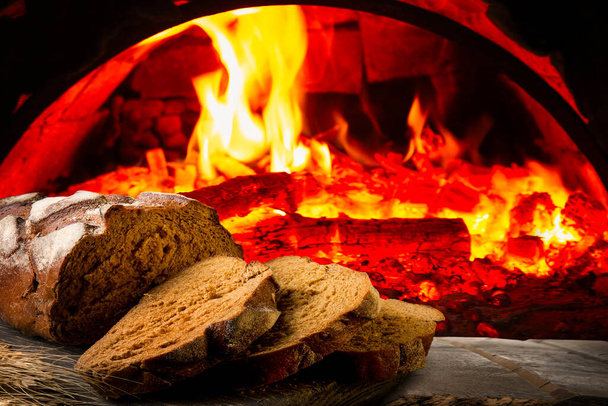 Pane fresco su uno sfondo di vecchio forno in mattoni pieno di legna da ardere - Foto, immagini