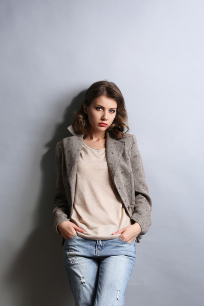 Portrait of beautiful model in jeans and jacket on gray background - Fotoğraf, Görsel