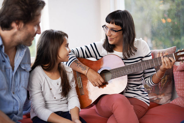 Μητέρα, μουσική και παίζοντας κιθάρα για την οικογένεια στο σπίτι, χαλαρώνοντας και απολαμβάνοντας μαζί στον καναπέ. Παράσταση, πατέρας και παιδί με γυναίκα στο σαλόνι, ψυχαγωγία και χαρά με μουσικό όργανο. - Φωτογραφία, εικόνα