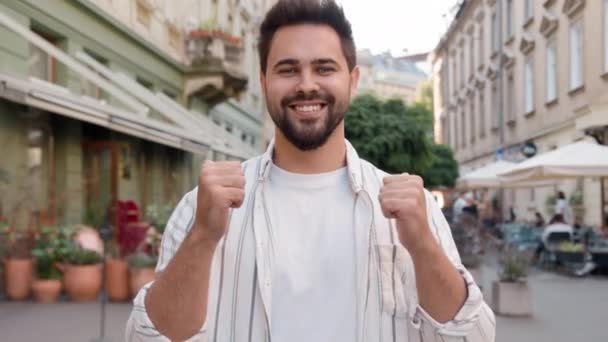 Young Caucasian man posing smiling showing thumb up happy joyful cheerful guy enjoying toothy dental smile satisfaction funny urban city outside businessman friendly male model gesture positive sign - Footage, Video