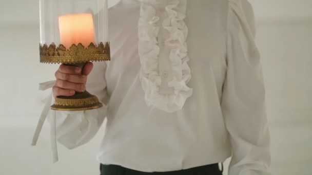 Person in elegant attire holding a candle lamp, with focus on the ruffled shirt and vintage lamp during the morning - Footage, Video