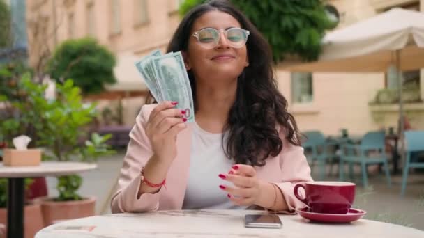 Glücklich lächelnd lachen erfolgreiche indische arabische ethnische Frau Studentin weibliche Mädchen Geschäftsfrau mit Show Bargeld Zahlung Dollar Business Investor Startup sitzt Café Tisch Straße Stadt außerhalb - Filmmaterial, Video