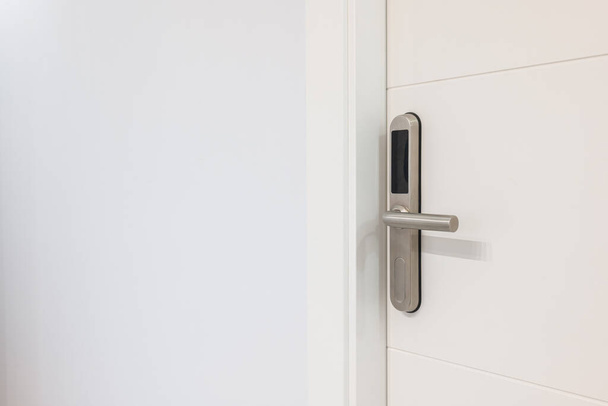 Κλείσιμο εισόδου λευκής πόρτας με ηλεκτρονική κλειδαριά νεκροψίας. Μια ηλεκτρονική μονάδα με οθόνη είναι ενσωματωμένη σε μεταλλική λαβή. Άνοιγμα θυρών με πλαστική κάρτα με μικροτσίπ ή ψηφιακό κωδικό - Φωτογραφία, εικόνα