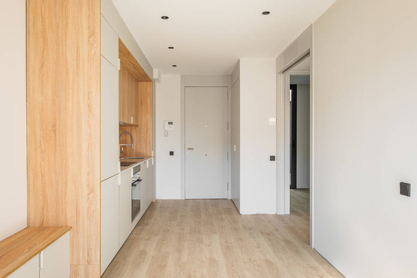 Egyszerű kis moduláris konyha a fal mentén stúdió apartman mellett a bejárati ajtó. Bútor minimalizmus sok szekrények, sütő és indukciós tűzhely a főzés finom ételek - Fotó, kép