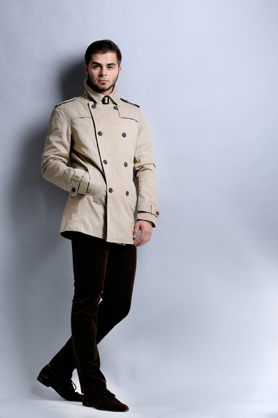 灰色の背景にコートを着た若い男 - 写真・画像