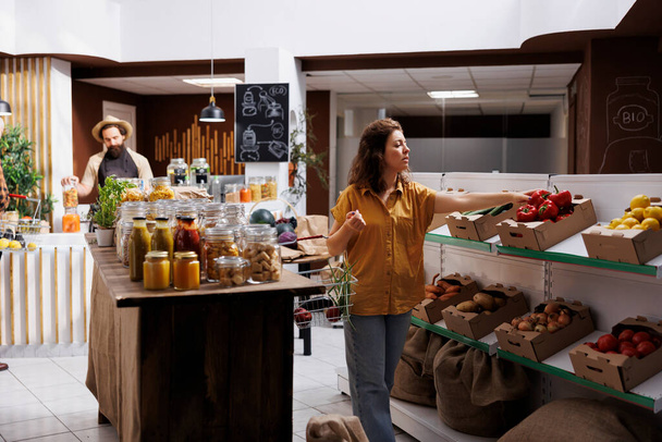 Зеленая живая женщина в магазине нулевых отходов заинтересована в покупке натуральных овощей с высокой питательной ценностью. Клиент делает покупки в устойчивом местном супермаркете - Фото, изображение
