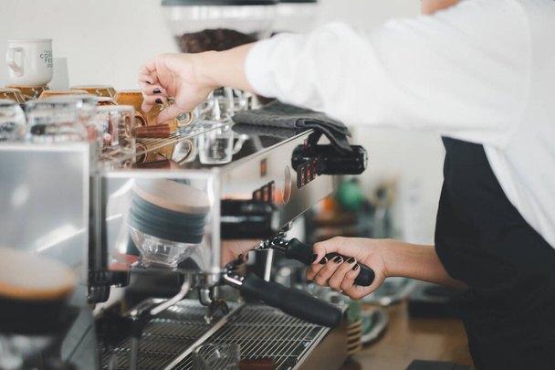Un barista experto en un delantal negro opera expertamente una máquina de café expreso, centrándose en la elaboración de la taza perfecta de café. - Foto, Imagen