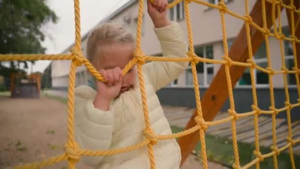 Malá holka lezení lano v bundě podzim město mimo hřiště dětství fyzické cvičení dítě dcera žák elementární věk zábava hrát pohyb energické tvrdé dovednosti denní sporty - Záběry, video