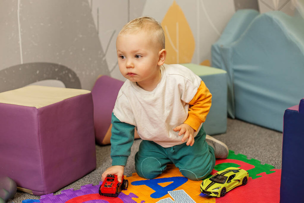 Bambino concentrato che gioca con auto giocattolo rosse e gialle su un tappeto da gioco multicolore, migliorando la coordinazione e le abilità di gioco. - Foto, immagini