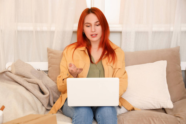 Молода жінка з ноутбуком відео балакає на дивані вдома - Фото, зображення