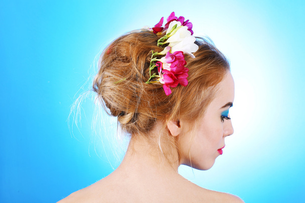 Portrait of young woman with flowers in hair on blue background - Foto, Imagem