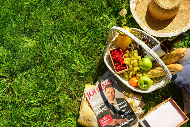 Zestaw na romantyczny piknik z wiklinowym koszem pełnym smacznych potraw i napojów na trawie w parku - Zdjęcie, obraz