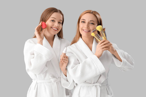 Nuori nainen ja hänen äitinsä kylpytakit meikki tarvikkeet valolla taustalla - Valokuva, kuva