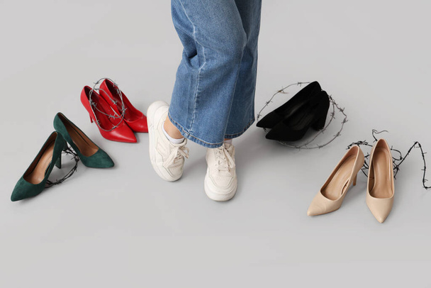 灰色の背景にスニーカーを着用した靴を持つ若い女性. 不快な靴のコンセプト - 写真・画像