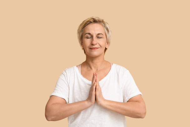 Portret van mediterende volwassen vrouw op beige achtergrond - Foto, afbeelding