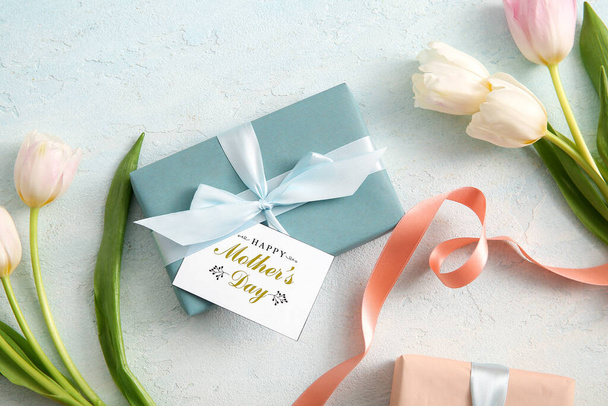 Tarjeta con texto FELIZ DÍA DE LA MADRE, cajas de regalo y flores de tulipán sobre fondo claro - Foto, Imagen