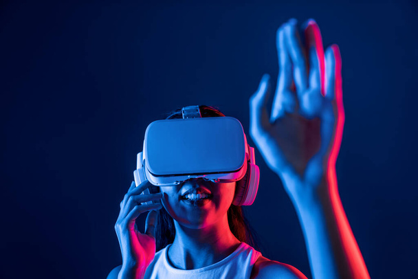 Mujer inteligente de pie en cyberpunk neón luz desgaste VR auriculares que conectan metaverso, futurista tecnología de la comunidad del ciberespacio. Mujer elegante uso de tocar a mano generado objeto virtual. Alucinaciones. - Foto, imagen