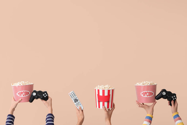 Many hands with buckets of popcorn, TV remote and game pads on beige background - Photo, Image