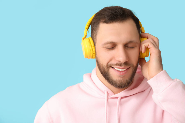 Νεαρός άνδρας με σύγχρονα ακουστικά σε μπλε φόντο - Φωτογραφία, εικόνα