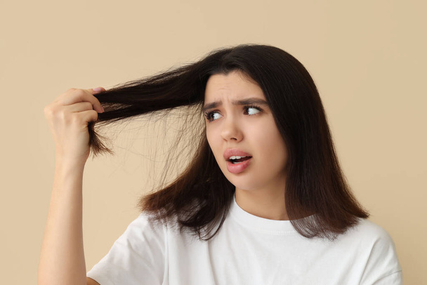Stressed young woman with dandruff problem examining her hair on beige background - Photo, Image